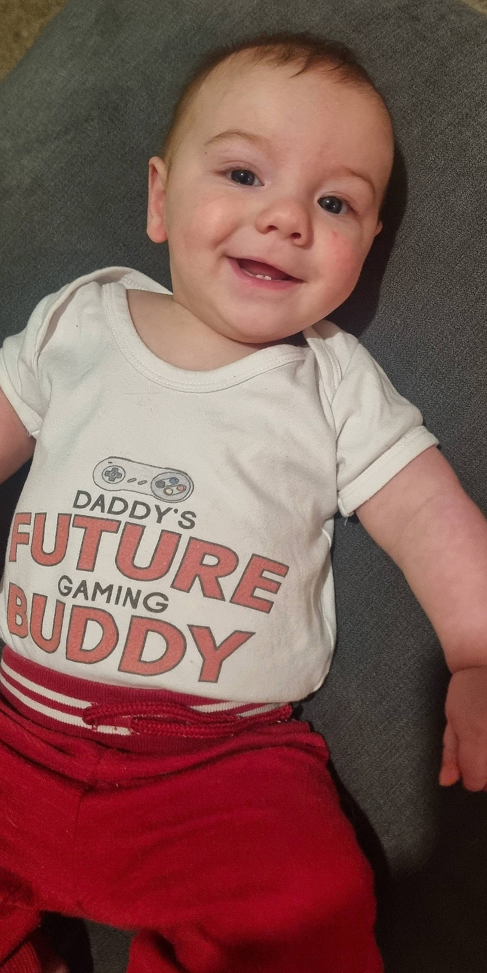 Orlando joined the competition — help win amazing prizes! apparel, baby, casual_clothing, child, closeup, cute, face, gaming_controller, happy, human, indoor, infant, lying_down, person, portrait, red_pants, smiling, text_on_clothing, white_shirt, young_child