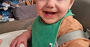Orlando is registered to the contest to win money with this photo: baby, child, crib, cute, face, food, furniture, green_bib, happy, high_chair, home, indoor, infant, messy, person, refrigerator, room, seated, smiling, young