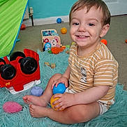 Orlando joined the competition — help win amazing prizes! toddler, child, smile, indoor, toy, plastic_ball, rug, striped_shirt, zebra_patch, floor, playroom, colorful, wooden_blocks, tent, car_toy, happy, sitting, person, furniture, foot