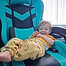 child, toddler, boy, smiling, happy, portrait, sitting, lounging, chair, gaming_chair, turquoise, yellow_clothing, pajamas, snack, indoors, window, daylight, playful, relaxed, close_up