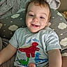 Orlando is registered to the contest to win money with this photo: toddler, child, smile, teeth, tshirt, dinosaur, pillow, cloud_pattern, blanket, indoor, happy, cute, portrait, baby, person, clothing, sitting, head, face, skin