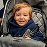 child, toddler, baby, smiling, happy, portrait, stroller, car_seat, harness, buckled, blue_clothing, hoodie, red_hair, brown_eyes, indoors, close_up, seated, infant, safe, photography