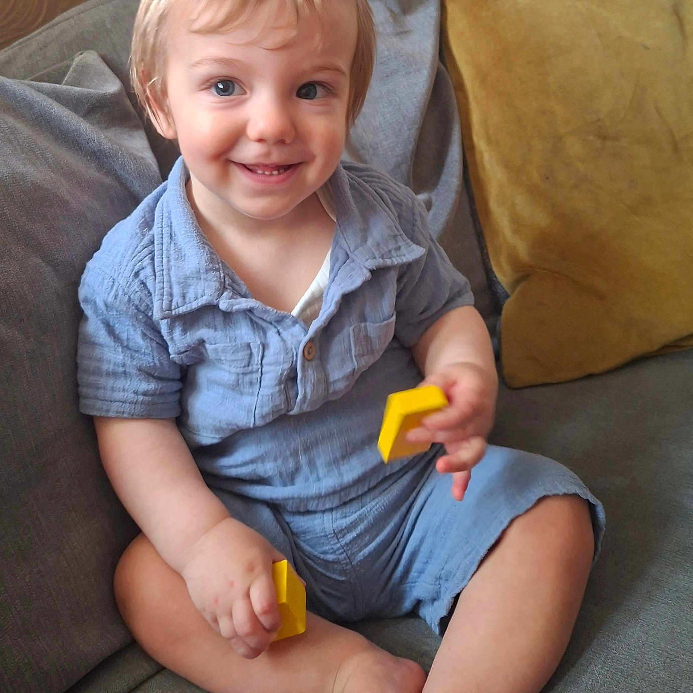 Orlando is registered to the contest to win money with this photo: toddler, child, smiling, blue_eyes, short_hair, blue_shirt, yellow_blocks, couch, gray_cushion, yellow_cushion, indoor, happy, sitting, barefoot, cute, portrait, playful, cozy, home, person