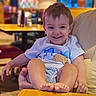 background, blurred, cafe, chair, child, clothing, face, feet, hair, hand, happy, indoor, person, restaurant, seated, shorts, smile, table, toddler, tshirt