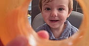 Orlando is registered to the contest to win money with this photo: baby, background, chair, child, clothing, face, furniture, hair, hand, happy, indoor, light, orange_ring, person, playful, portrait, skin, smiling, table, toddler