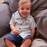 Orlando is registered to the contest to win money with this photo: baby, blanket, casual_clothing, child, couch, cozy, cute, feet, furniture, happy, indoor, living_room, person, portrait, seated, shirt, shorts, smiling, toddler, young_child