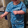 barefoot, blue_clothing, carpet, child, couch, cute, face, fish_pattern, happy, home_interior, indoor, living_room, motion, person, shirt, shorts, smiling, standing, toddler, young_child
