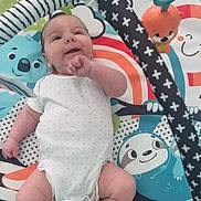 Orlando is registered to the contest to win money with this photo: baby, infant, play_mat, toy, colorful, smiling, lying_down, onesie, patterned, soft_toys, cute, child, indoor, happy, small_hands, small_feet, animal_print, playtime, comfort, nursery