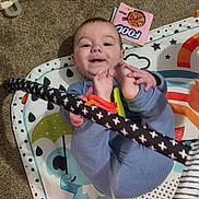 Orlando joined the competition — help win amazing prizes! baby, child, blue_pajamas, play_mat, carpet, toy, book, smiling, happy, infant, feet, hands, colorful, indoor, person, cute, playful, floor, patterned, young