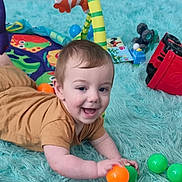 Orlando joined the competition — help win amazing prizes! baby, child, toy, play, floor, rug, colorful, ball, smile, happy, indoor, onesie, crawling, baby_gym, soft, orange_ball, green_ball, car_toy, plush, playroom