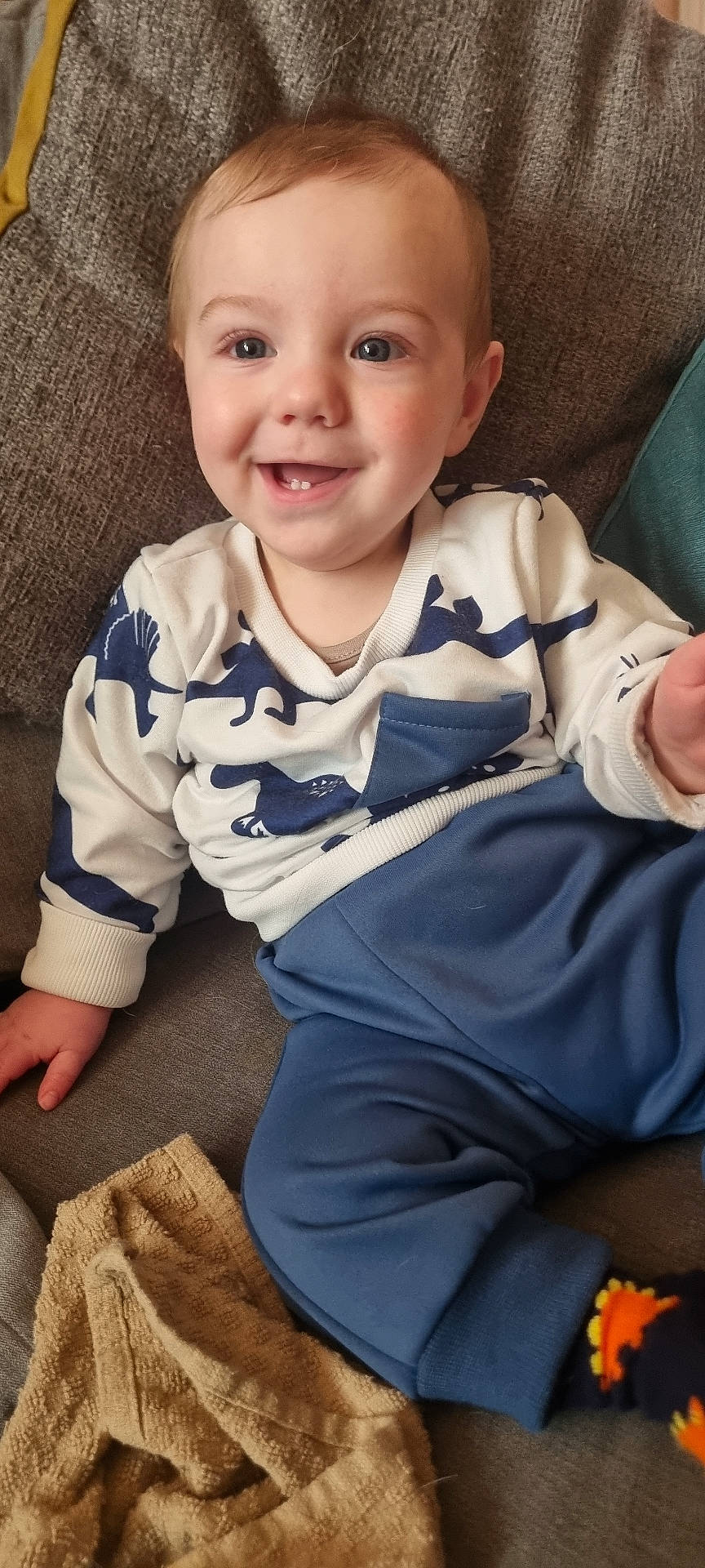 Orlando is registered to the contest to win money with this photo: baby, child, clothing, couch, cozy, cute, dinosaur_pattern, face, happy, home, indoor, pants, person, portrait, sitting, smiling, sweater, toddler, towel, young_child