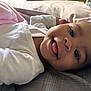baby, smile, tongue, white_clothing, blanket, bed, pillow, infant, face, cheek, lying_down, cute, expression, skin, head, happy, indoors, soft_light, closeup, person