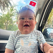 Rafael is registered to the contest to win money with this photo: baby, child, smiling, curly_hair, striped_shirt, bunny_design, car_interior, window, trees, sunlight, happy, face, cute, indoors, seat, reflection, clothing, young_child, portrait, seatbelt_clip