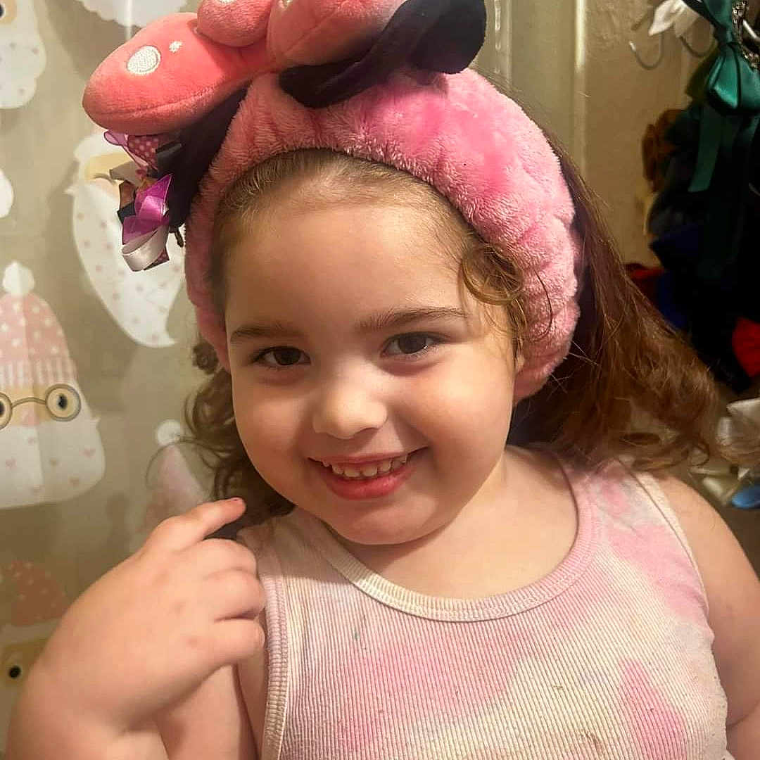 Wynter is registered to the contest to win money with this photo: background, bathroom, child, clothing, curly_hair, cute, decor, expression, face, furniture, hand, happy, indoor, person, pink_headband, playful, portrait, smile, tank_top, young_child