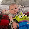 Christopher is registered to the contest to win money with this photo: baby, smiling, plush_toy, bed, pillow, blanket, indoor, child, person, cute, soft_toy, happy, lying_down, cozy, furniture, fabric, hand, head, room, sleepwear