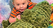 Christopher joined the competition — help win amazing prizes! baby, child, toy, plush, crocodile, green, striped_shirt, curious, face, indoor, colorful_background, soft_texture, smiling, young, cute, playful, person, portrait, infant, cuddly