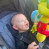 Christopher is registered to the contest to win money with this photo: baby, blue_eyes, black_clothing, child, colorful_toy, delighted, expression, face, hand, infant, light, plush_toy, reaching, safety_harness, stroller, toy, young_child, outdoor_light, happy, smiling