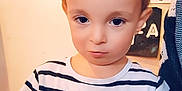 Kenzo participe au concours pour gagner de l'argent avec cette photo : child, boy, striped_shirt, indoor, wall_photos, pencil, heart_emoji, young_child, portrait, serious_expression, yellow_speech_bubble, hand, short_hair, light_skin, background_decor, drawing, paper, casual_clothing, standing, closeup