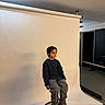 child, portrait, studio, backdrop, stool, seated, fashion, sweater, pants, shoes, indoors, photography, lighting, ceiling, roller_backdrop, serious_expression, dark_clothing, gray_pants, full_body, fashion_pose