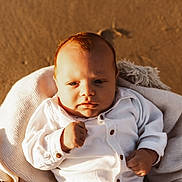 Sacha participe au concours pour gagner de l'argent avec cette photo : baby, infant, blanket, white_clothing, beach, sand, fist, portrait, sunlight, outdoor, cute, young_child, cozy, serious_expression, closeup, soft_texture, warm_light, child, person, nature