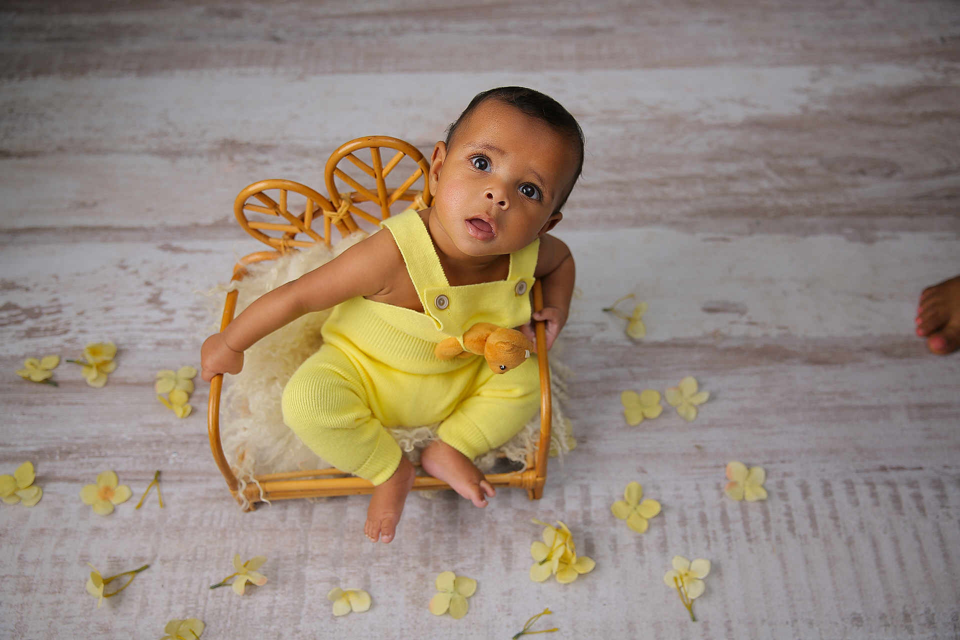Ethan joined the competition — help win amazing prizes! baby, infant, child, yellow_outfit, teddy_bear, wicker_chair, rattan_basket, cozy_blanket, curious_expression, big_eyes, portrait, studio_shot, props, flower_petals, wooden_floor, bare_feet, button_straps, soft_toys, sitting, cute