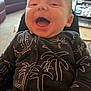baby, infant, smiling, clothing, onesie, palm_tree_pattern, indoor, living_room, furniture, couch, carpet, person, happy, portrait, child, cute, young, head, expression, seated