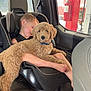 black_clothing, car_interior, car_seat, child, cozy, curly_fur, daytime, dog, fire_extinguisher, foot, gas_station, pet, puppy, resting, seat, seatbelt, sleeping, vehicle, window, young_child