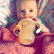 Meadow Rose joined the competition — help win amazing prizes! baby, child, face, blue_eyes, blanket, bottle, sippy_cup, floral_pattern, pink, green_clothing, bed, cute, infant, hands, lying_down, soft_texture, portrait, indoors, feeding, cozy