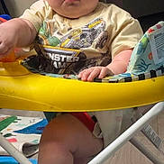 Malachi joined the competition — help win amazing prizes! baby, infant, child, portrait, serious_expression, sitting, activity_jumper, yellow, toy, indoor, play_area, graphic_shirt, bare_legs, face, eyes, hands, furniture, home, photograph, colorful