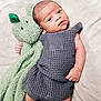 baby, infant, plush_toy, knitted_clothing, gray_outfit, green_bunny, blanket, soft_texture, cute, lying_down, child, newborn, cozy, portrait, indoors, hand, face, eyes, expression, resting