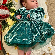 Reyna joined the competition — help win amazing prizes! baby, velvet_dress, blanket, golden_hearts, christmas_decoration, greenery, infant, foot, hand, face, curly_hair, carpet, indoors, plush, cute, holiday, decor, portrait, child, soft