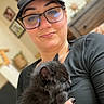 Mr Houdini joined the competition — help win amazing prizes! person, cat, kitten, black_cat, glasses, cap, indoor, portrait, smile, holding, pet, furniture, blurred_background, hand, face, black_clothing, nail_polish, nose_ring, cozy, cute