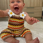 Martha participe au concours pour gagner de l'argent avec cette photo : baby, child, smiling, happy, sitting, colorful_clothing, zigzag_pattern, flower_applique, barefoot, indoor, rug, wooden_cabinet, cute, excited, portrait, infant, playful, bright, cheerful, person