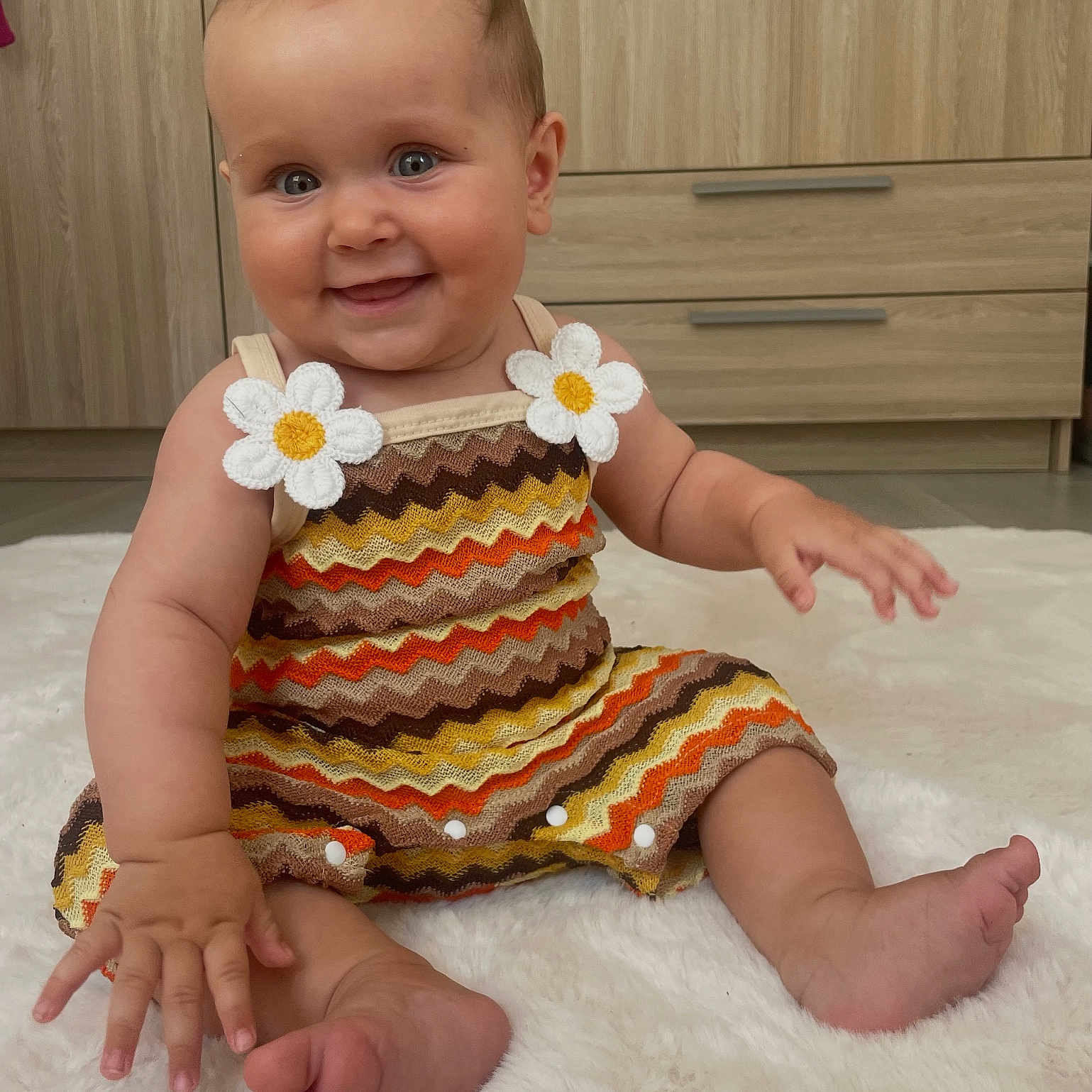 Martha a rejoint le concours — aidez-le/la à gagner de superbes lots ! baby, barefoot, child, colorful_clothing, cute, daisy_applique, dress, eyes, fluffy_rug, hand, happy, indoor, infant, person, portrait, sitting, skin, smiling, wooden_furniture, zigzag_pattern