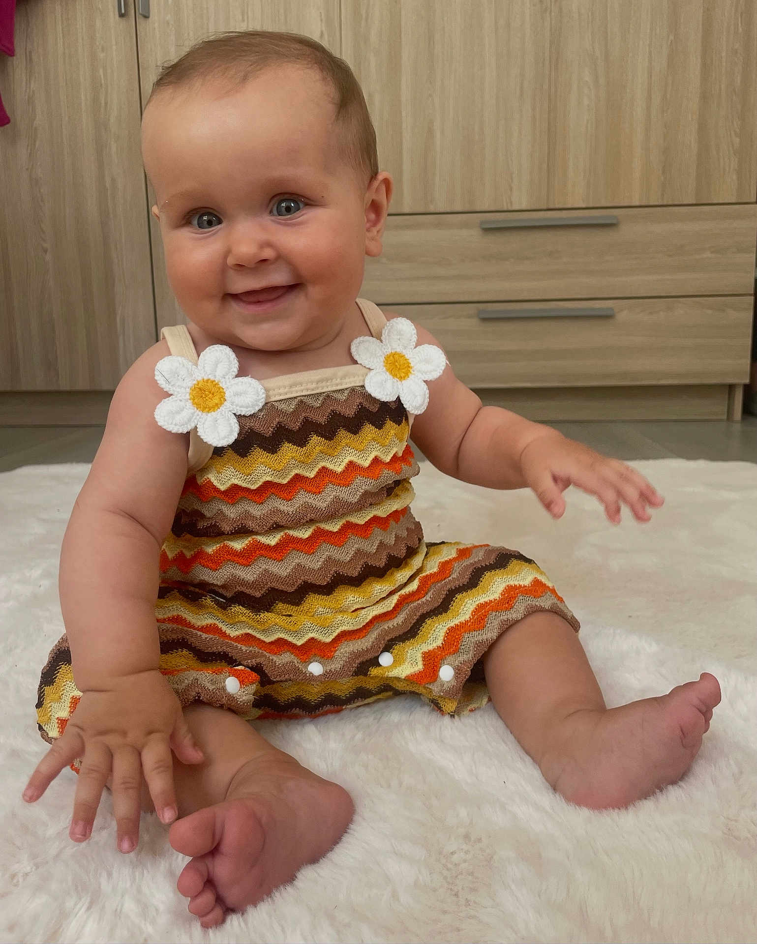 Martha a rejoint le concours — aidez-le/la à gagner de superbes lots ! baby, child, smiling, sitting, dress, colorful_clothing, daisy_applique, zigzag_pattern, fluffy_rug, barefoot, indoor, wooden_furniture, cute, happy, portrait, person, infant, skin, eyes, hand
