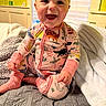 baby, bed, blanket, child, cozy, cute, dinosaur_pattern, face, happy, home, indoor, infant, pajamas, person, portrait, sitting, smiling, soft, warm, young