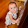 baby, child, toddler, standing, barefoot, face, portrait, smiling, curious, indoor, wooden_floor, furniture, home, dress, floral_clothing, hands, feet, warm_lighting, photography, family_photo