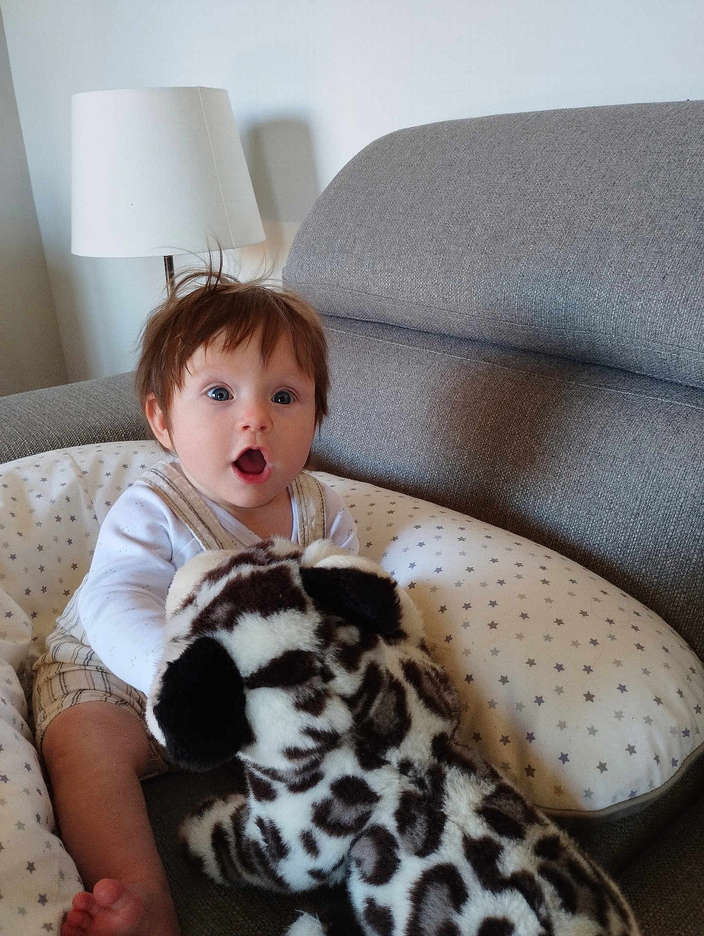 Léon a rejoint le concours — aidez-le/la à gagner de superbes lots ! baby, child, stuffed_animal, plush_toy, couch, pillow, indoor, surprised, expression, face, hair, white_clothing, patterned_pillow, seated, infant, soft_toy, home, furniture, cute, curious