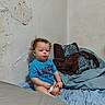 Liam is registered to the contest to win money with this photo: bed, bedding, bedroom, blanket, blue_shirt, child, clothing, face, green_toy, indoor, peeling_paint, photograph, pillows, portrait, red_hair, serious_expression, sitting, toddler, toy, wall