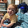 Liam is registered to the contest to win money with this photo: baby, bed, bedroom, blanket, brown_hair, child, clothing, colorful_bedding, curly_hair, face, furniture, home, indoors, infant, portrait, sitting, smiling, teeth, window, yellow_shirt