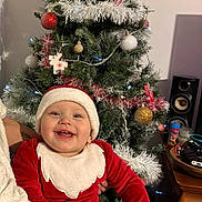 Ezio participe au concours pour gagner de l'argent avec cette photo : baby, child, christmas_tree, santa_claus_costume, holiday, smiling, tattoo, person, indoor, decorations, ornaments, tree_lights, festive, red_clothing, white_trim, happy, holiday_spirit, celebration, seasonal, holding