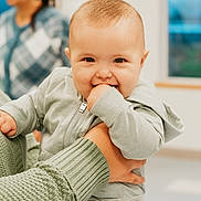 Ricardo joined the competition — help win amazing prizes! baby, child, smiling, hoodie, hand, adult_hand, indoor, person, woman, blurred_background, window, light, sweater, holding, cute, happy, face, infant, playful, clothing