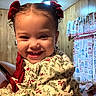 Zeliylah is registered to the contest to win money with this photo: child, toddler, smile, happy, face, hair_bow, red_bow, curly_hair, indoor, wood_paneling, curtains, patterned_curtains, clothing, floral_pattern, person, portrait, baby, cute, joyful, closeup