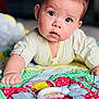 Mia is registered to the contest to win money with this photo: baby, infant, child, drool, face, eyes, quilt, toy, hand, clothing, lying, curious, colorful, soft_toy, indoor, person, closeup, portrait, cute, young