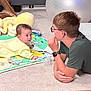 Mia is registered to the contest to win money with this photo: baby, child, young_person, carpet, toys, exercise_ball, glasses, yellow_clothing, floor, indoor, interaction, curiosity, playtime, blanket, carpeted_floor, wood_floor, watch, glasses_frame, person, home