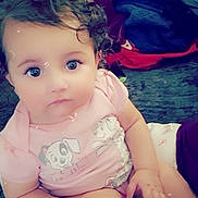 Gabriela is registered to the contest to win money with this photo: baby, child, clothing, curly_hair, cushion, cute, expression, face, floral_pattern, hand, indoor, large_eyes, leg, person, pink_shirt, portrait, puppy_cartoon, sitting, soft_light, toddler