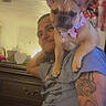 Nala joined the competition — help win amazing prizes! dog, french_bulldog, man, person, pet, portrait, indoors, bedroom, dresser, mirror, furniture, tattoo, blue_shirt, pink_bow, collar, sitting, shoulders, wrinkles, large_ears, companion