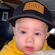 Luke joined the competition — help win amazing prizes! baby, child, face, cap, hat, yellow_hoodie, indoor, portrait, close_up, cute, person, clothing, headwear, young_child, eyes, skin, expression, casual, infant, indoors
