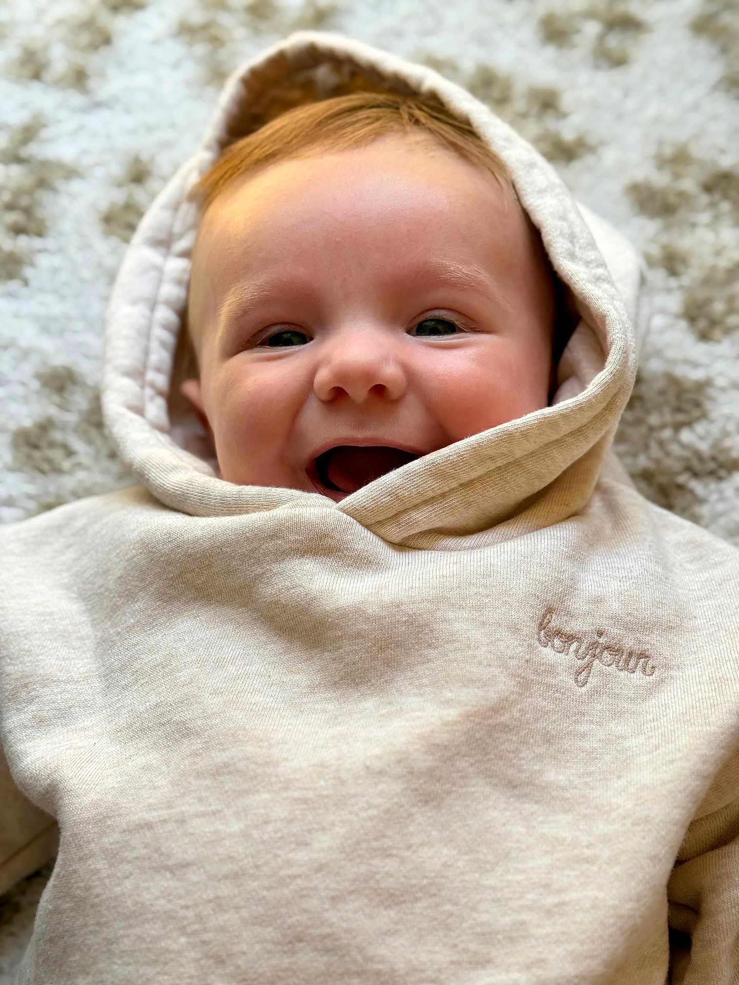 Mattéo a rejoint le concours — aidez-le/la à gagner de superbes lots ! baby, child, hoodie, smile, happy, face, infant, cozy, clothing, embroidery, textile, portrait, closeup, lying_down, carpet, soft_texture, cute, young, indoors, warm
