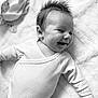 baby, infant, smiling, happy, lying_down, onesie, white_clothing, blanket, soft_texture, cute, child, portrait, indoor, head, face, young_child, joyful, spiky_hair, newborn, relaxed